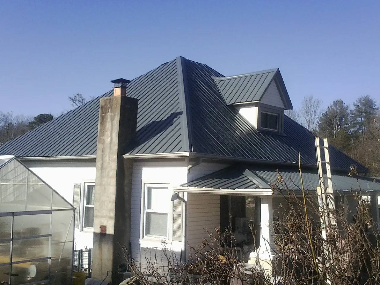 Dark blue standing seam metal roof on a white farmhouse with dormer — Slate & Tile Roof Repair by Roofing Brothers in Guthrie