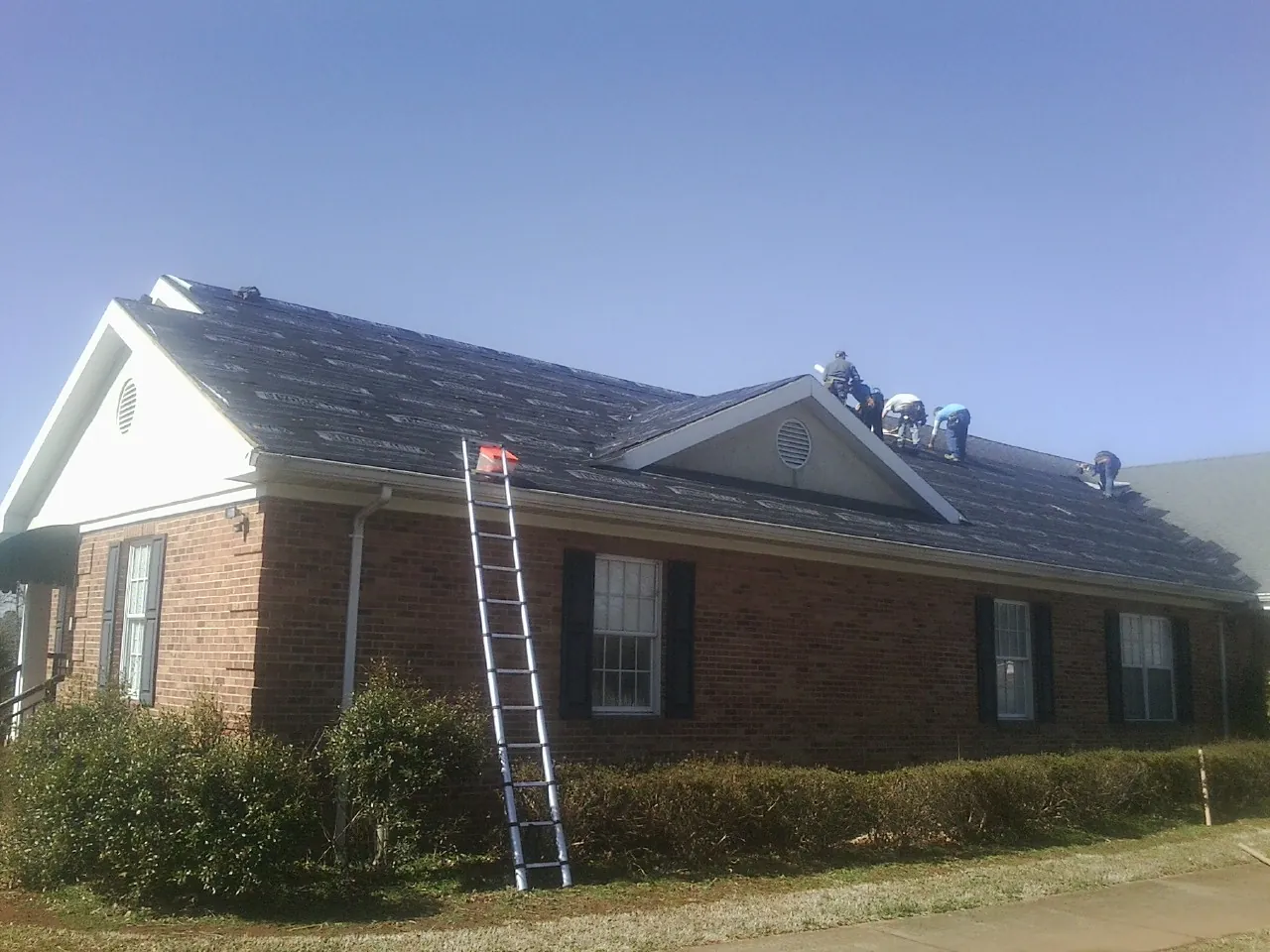 Crew tearing shingles off a brick ranch roof with a ladder set — Metal Roof Repair work by our crew in Guthrie