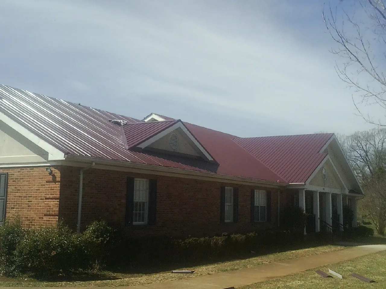 Red metal roof with gabled entries on a long brick building, from a Hail Damage Roof Repair job in Guthrie