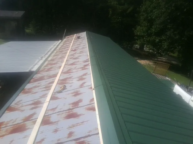 Old rusted panels beside newly installed green metal roofing — Wind Damage Roof Repair by Roofing Brothers in Guthrie