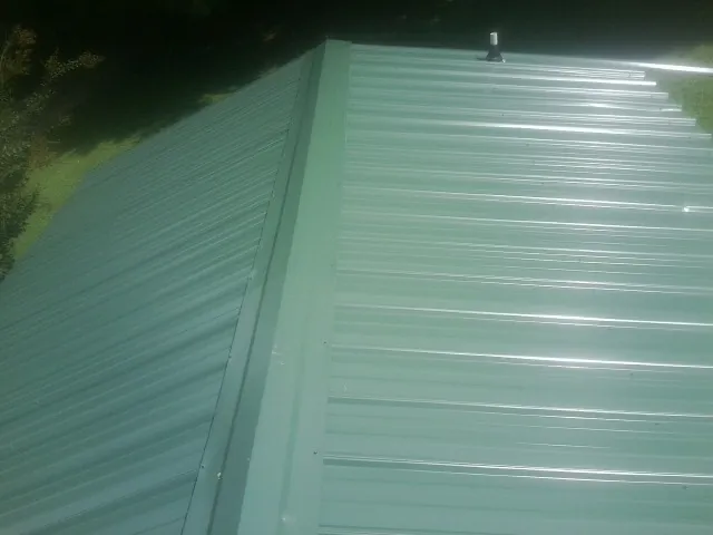 New green metal panels meeting at the ridge of a roof — Flat Roof Repair work by our crew in Guthrie