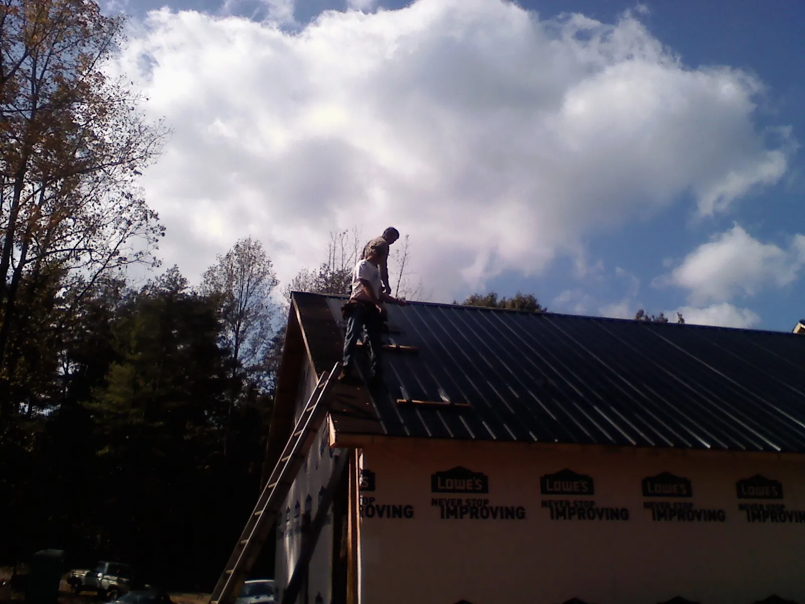 Roofer fastening dark metal panels high against a cloudy sky, from a Roof Inspection job in Guthrie