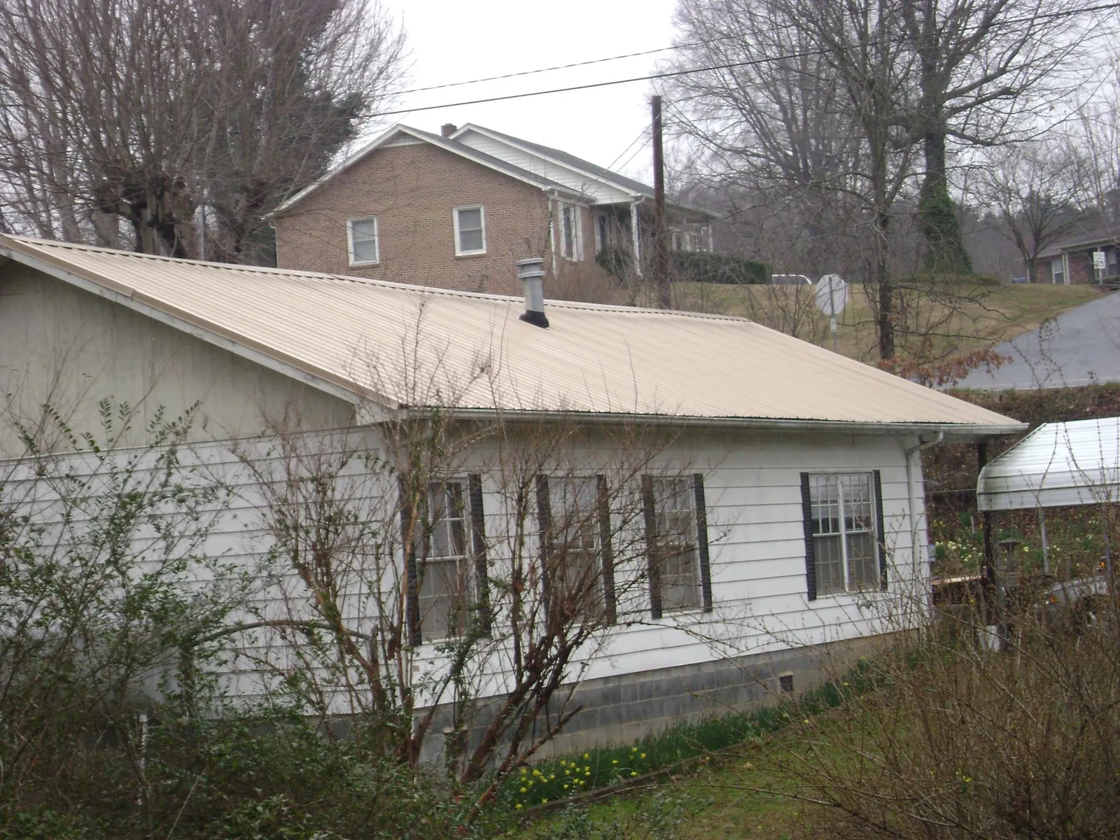 Tan metal roof on a white sided house set into a hillside — Commercial Roofing by Roofing Brothers in Guthrie
